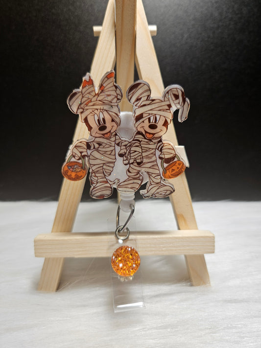 Retractable badge reel with Minnie and Mickey mummy figures and orange glitter charm