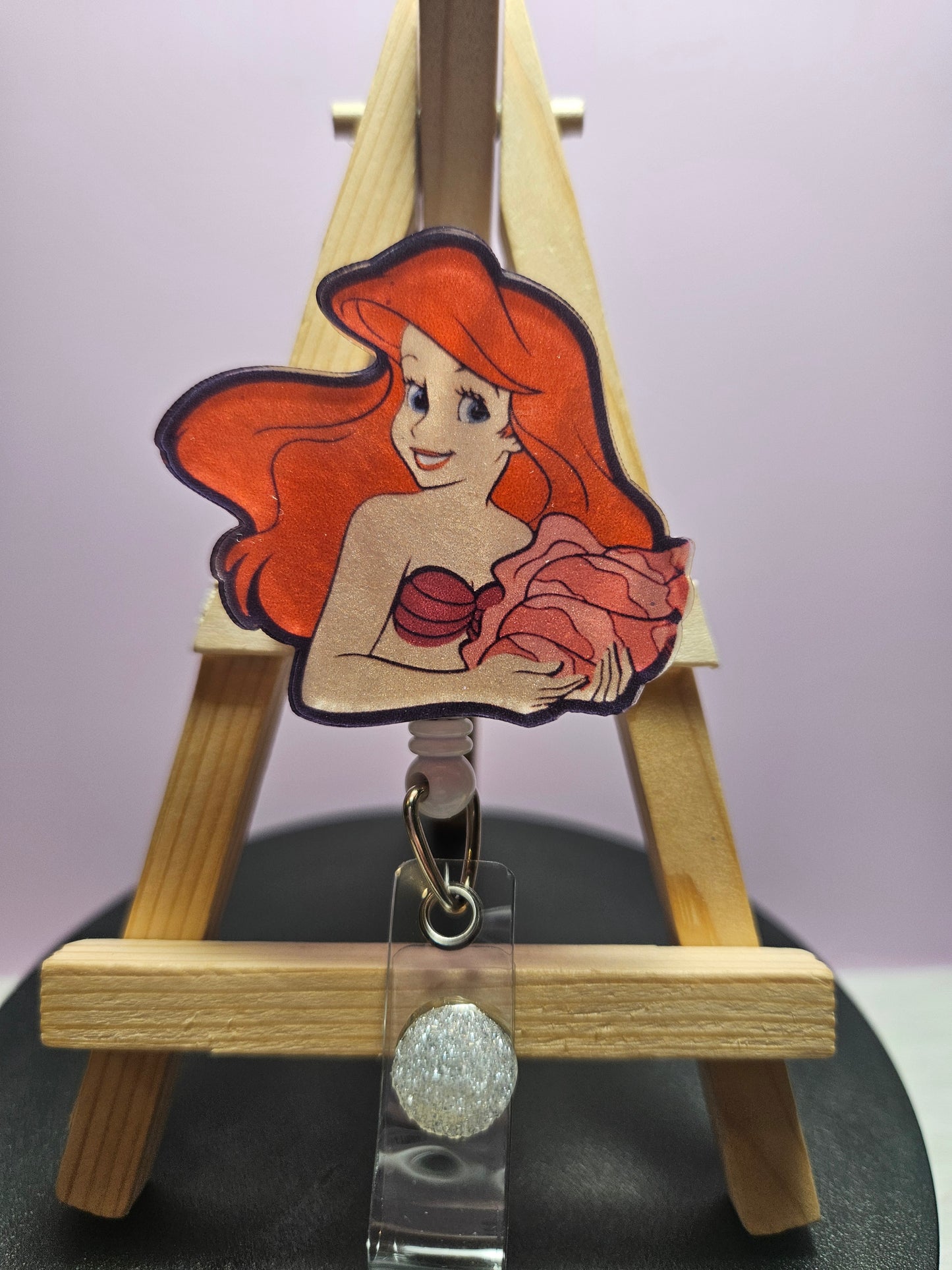 A retractable badge reel featuring an illustration of a mermaid character in vibrant colors attached to a clear acrylic holder.