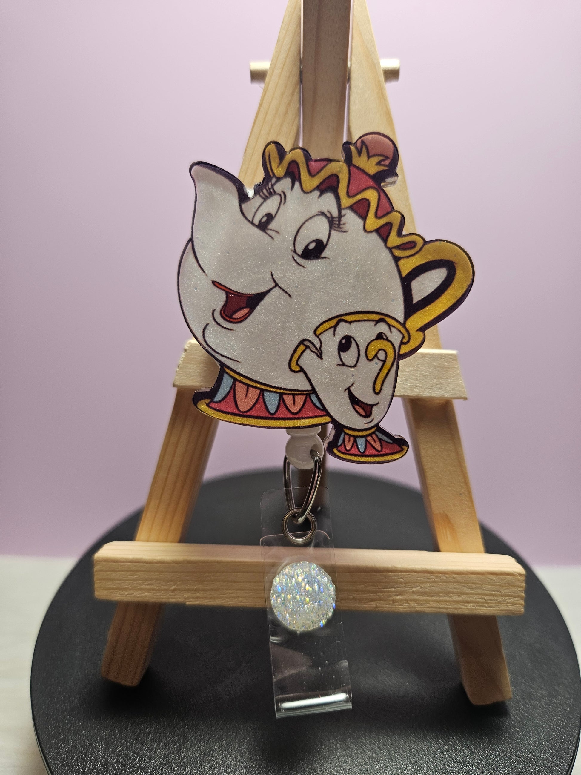 A retractable badge reel featuring a colorful character design, resembling a animated teapot, attached to a wooden display stand.