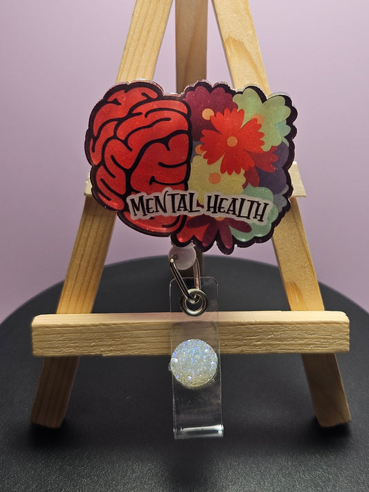 A retractable badge reel with a floral and brain design, labeled 'MENTAL HEALTH', displayed on a wooden easel.